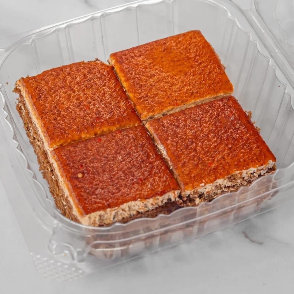 Four square pieces of dessert with a brown base and an orange, textured topping in a plastic container.