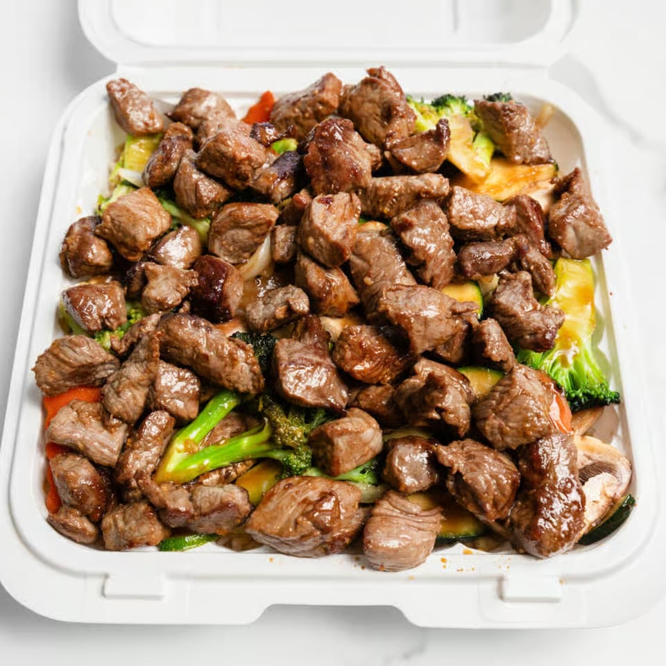 Hibachi steak and mixed vegetables, including broccoli, zucchini, and mushrooms, in a white takeout container.