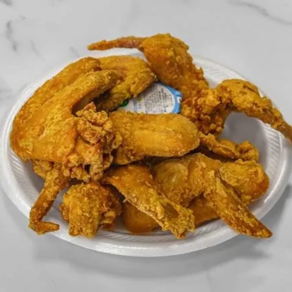 A white plate piled high with golden-brown fried chicken wings and a small cup of dipping sauce.