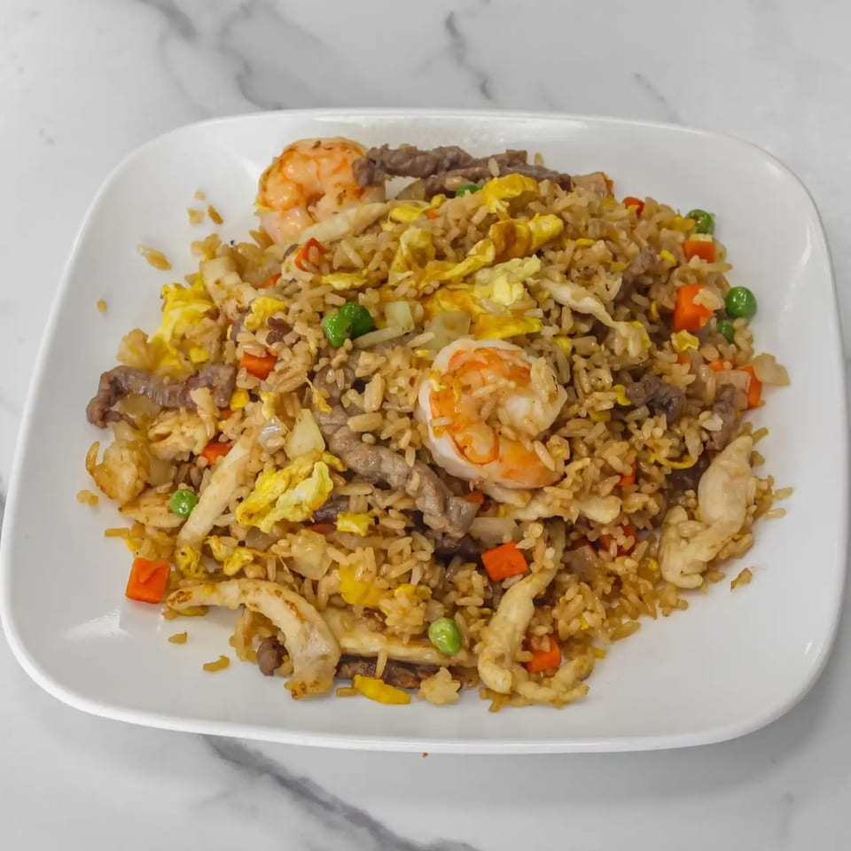A white plate filled with Aaron Wings & Hibachi fried rice, shrimp, beef, chicken, and vegetables.