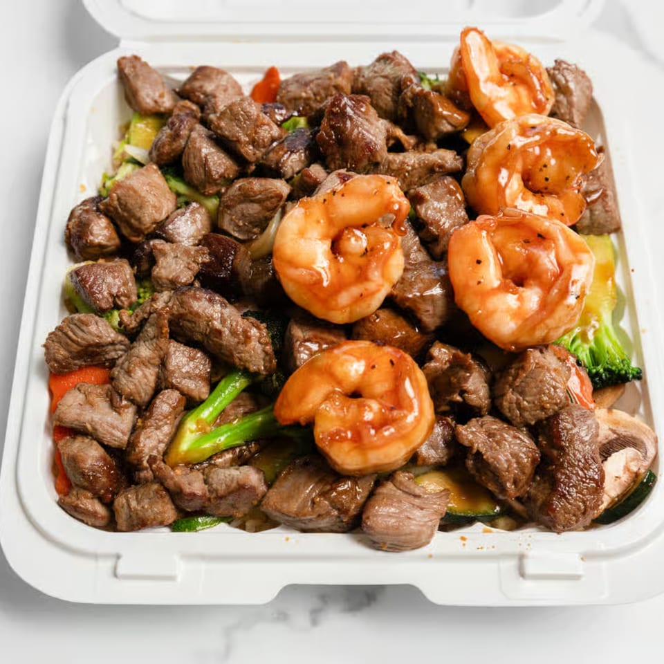Hibachi steak and shrimp with mixed vegetables in a white takeout container.