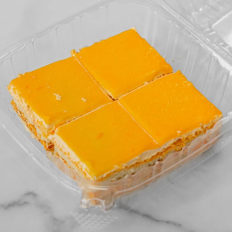 Four square pieces of mango cheesecake with a creamy filling in a clear plastic container.